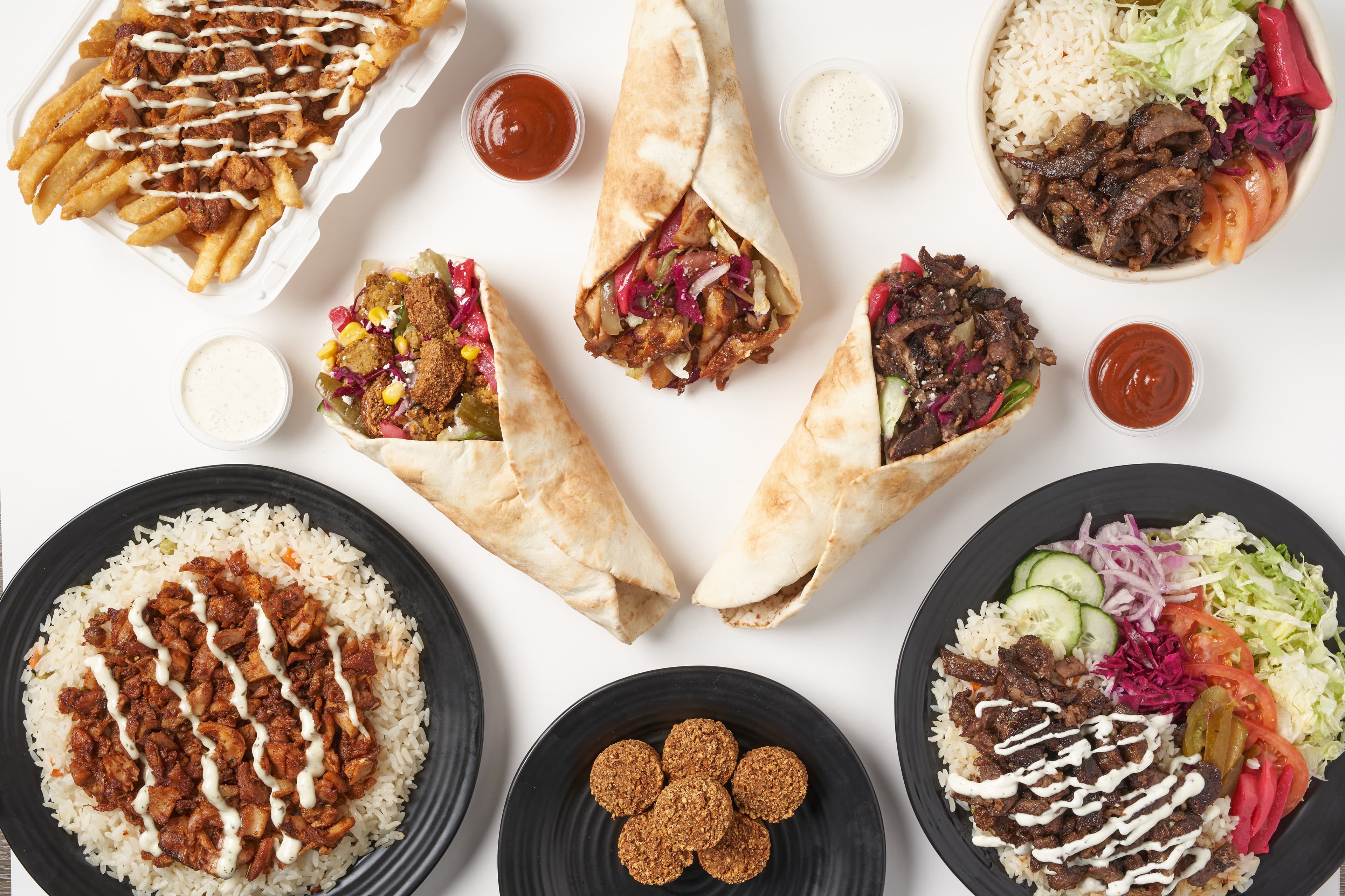 Overhead spread of Shawarma Moose catering — chicken and beef bowls, wraps, falafel, sauces